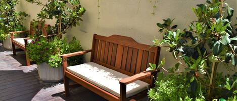 A wooden bench with a cushion, surrounded by potted plants and greenery.