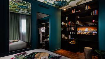 Habitación de hotel con cama, un espejo grande, una estantería y un televisor que muestra un paisaje urbano.