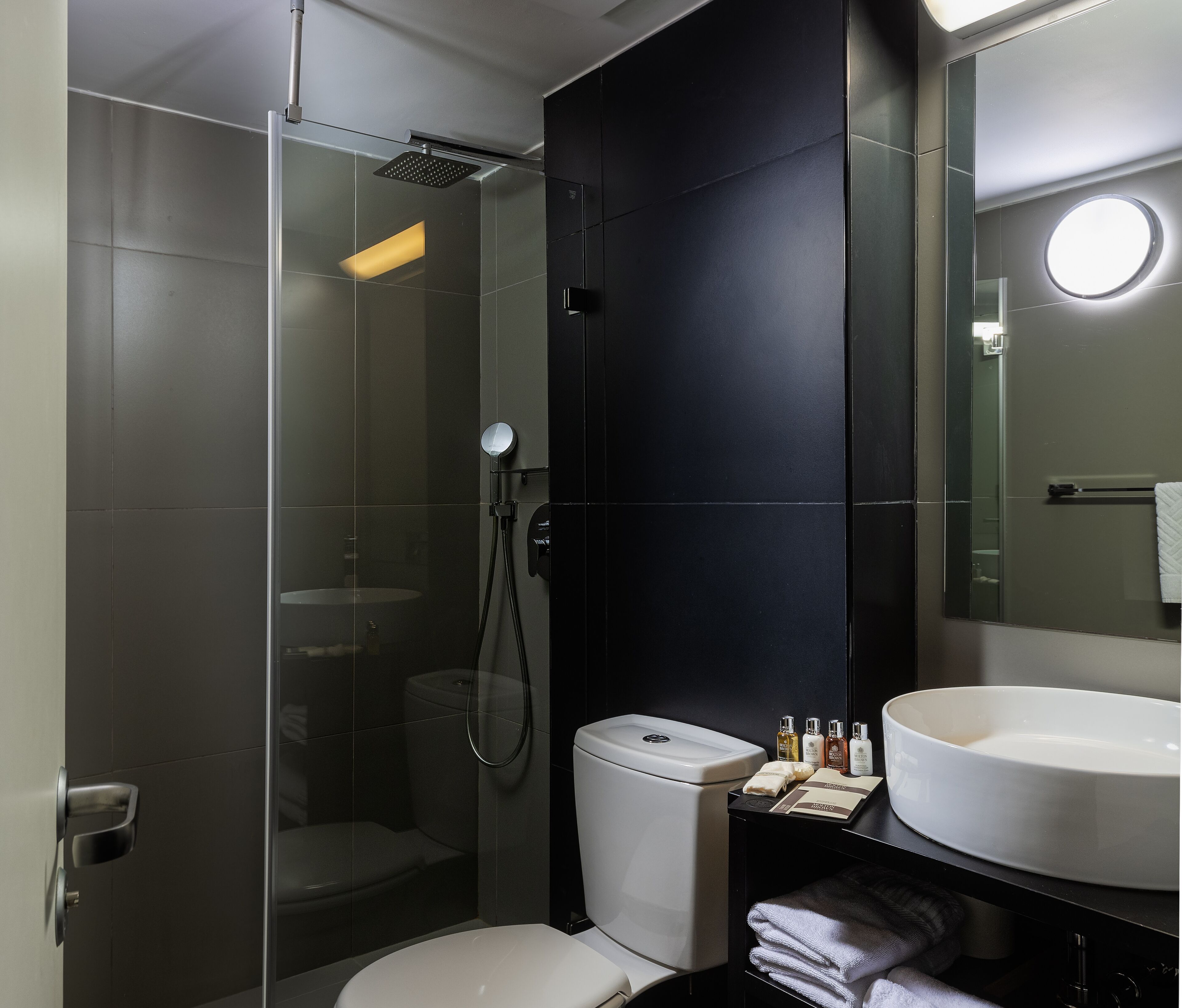 Ein modernes Badezimmer mit einer gläsernen Duschkabine, einer weißen Toilette und einem großen Waschbecken mit Pflegeartikeln.