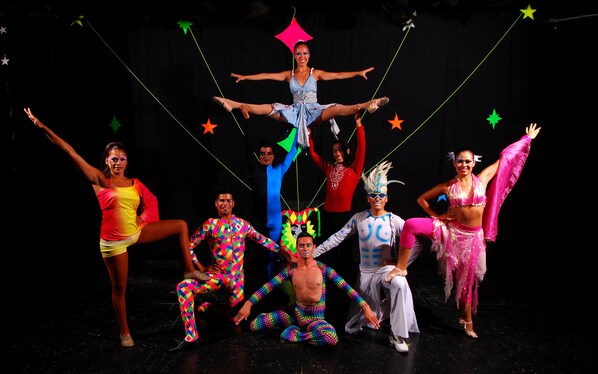 Un grupo de personas vestidas con trajes coloridos en un escenario con fondo negro y decoraciones de estrellas.