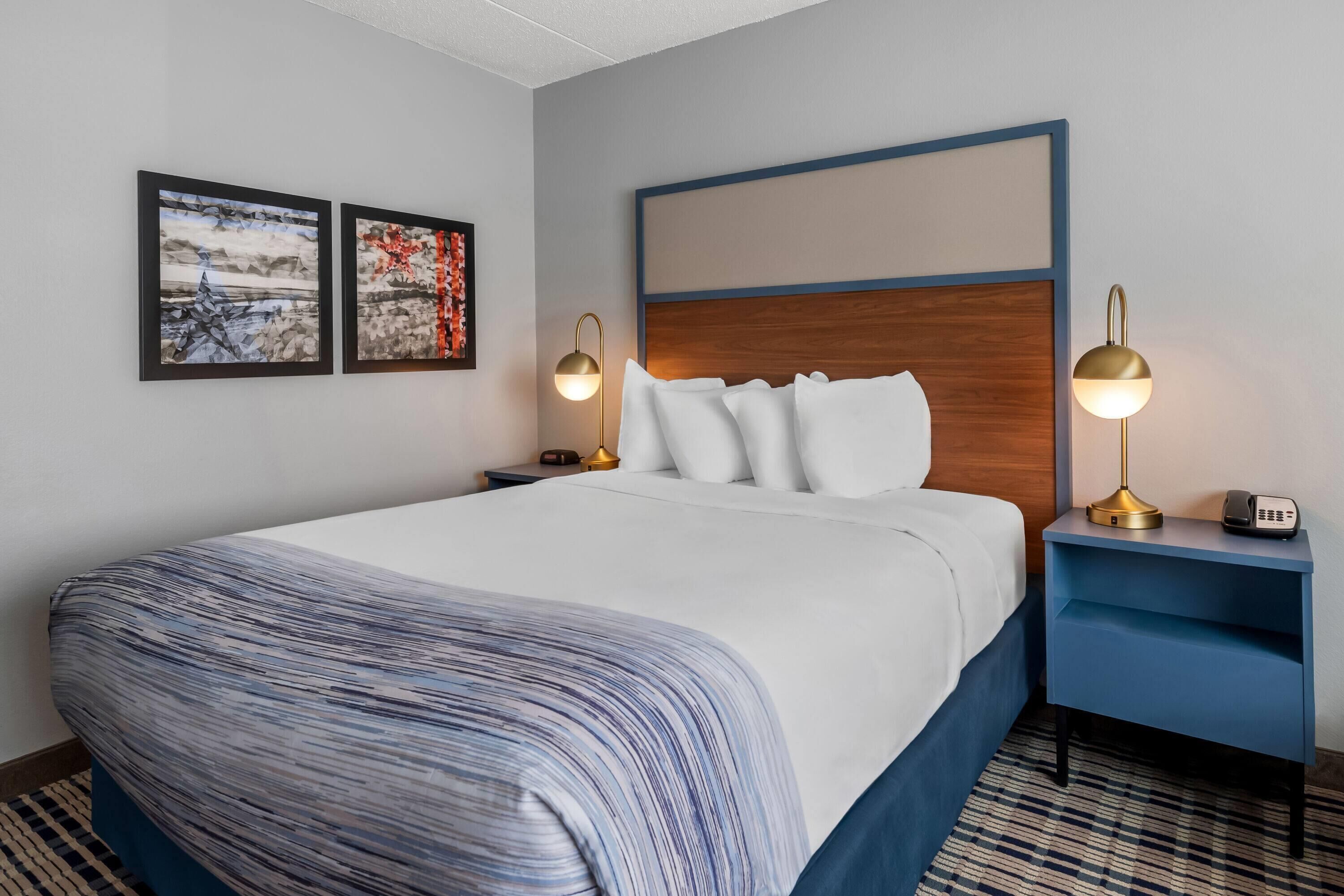 A hotel room with a large bed, two bedside lamps, a nightstand, and two framed pictures on the wall.