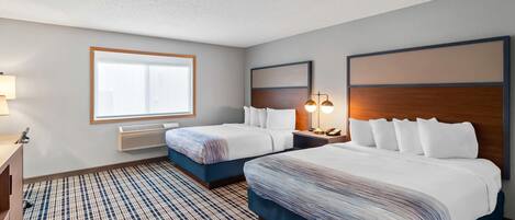 A hotel room with two beds, a large window, a heater, and a lamp.
