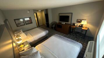 A hotel room with two beds, a desk, a TV, and a chair.