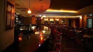 Una zona de bar con una barra curva, diversas opciones de asientos e iluminación colgante.