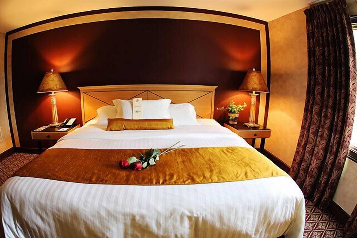 A hotel room with a large bed, two bedside tables with lamps, a sofa, and a decorative plant.