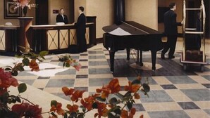 Un vestíbulo con mostrador de recepción, un piano de cola y flores decorativas.