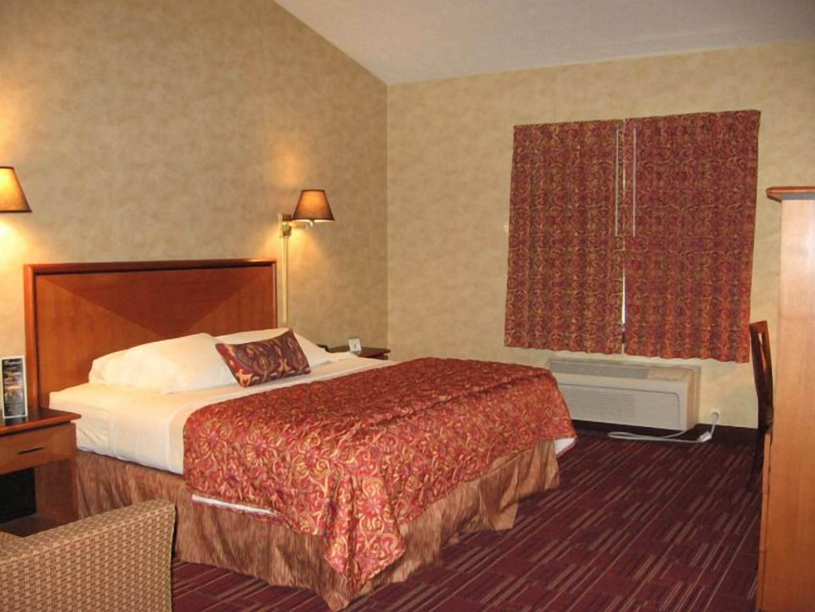 Ein Hotelzimmer mit einem großen Bett, zwei Nachttischlampen, einem Fenster mit gemusterten Vorhängen und einer Heizung.