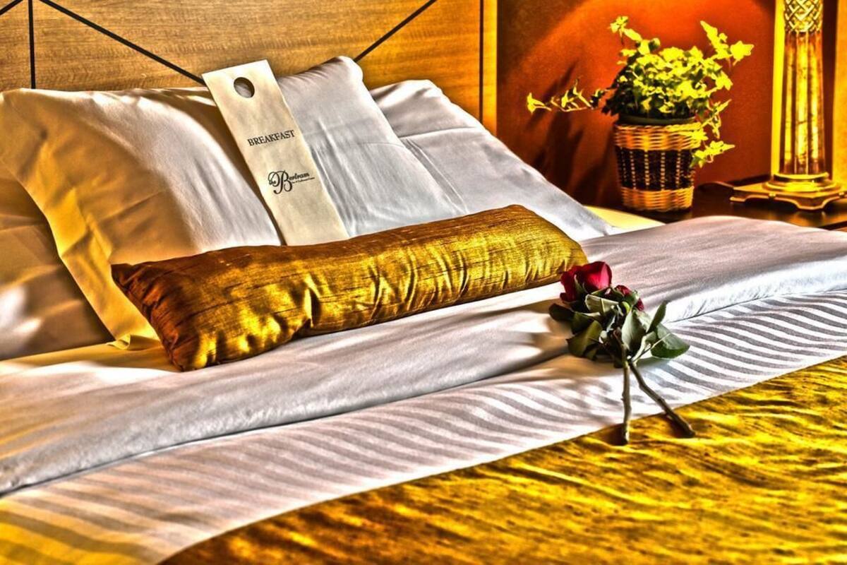 A neatly made bed with white linens, a gold-colored pillow, and a tag reading "Breakfast."