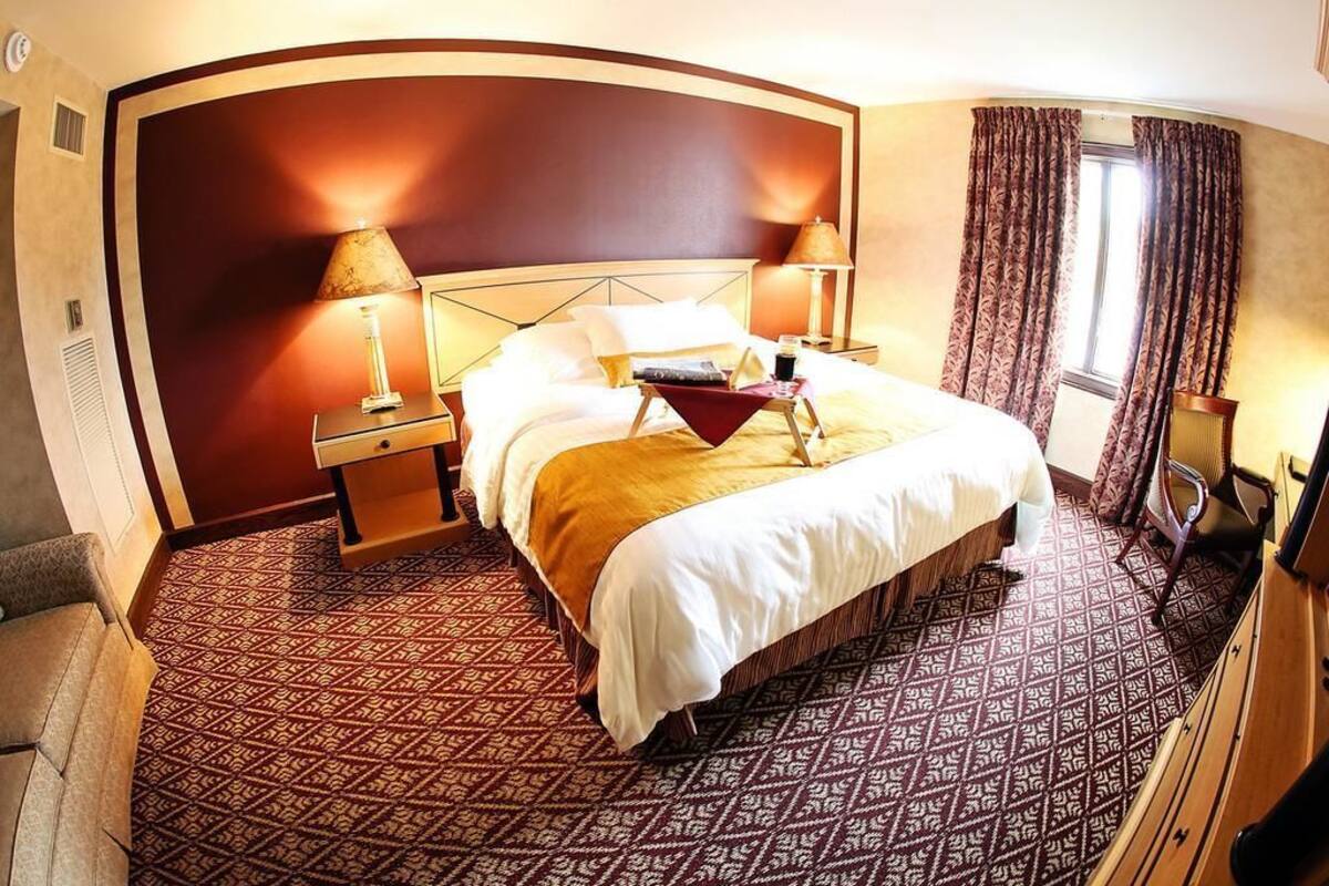 A hotel room with a large bed, two bedside tables, a desk, a chair, and a window with curtains.
