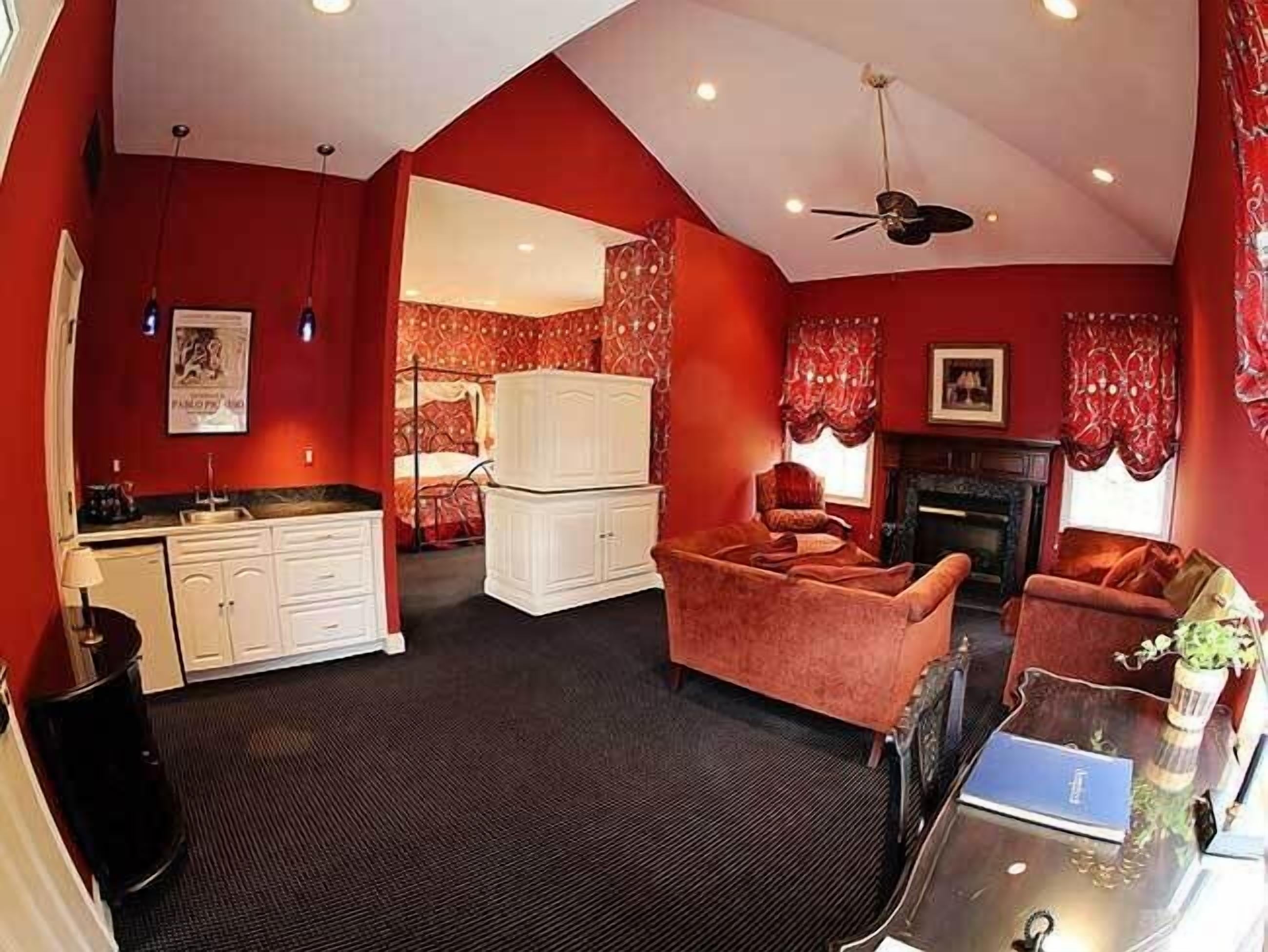A room with a kitchenette, a fireplace, a sofa, and a ceiling fan.