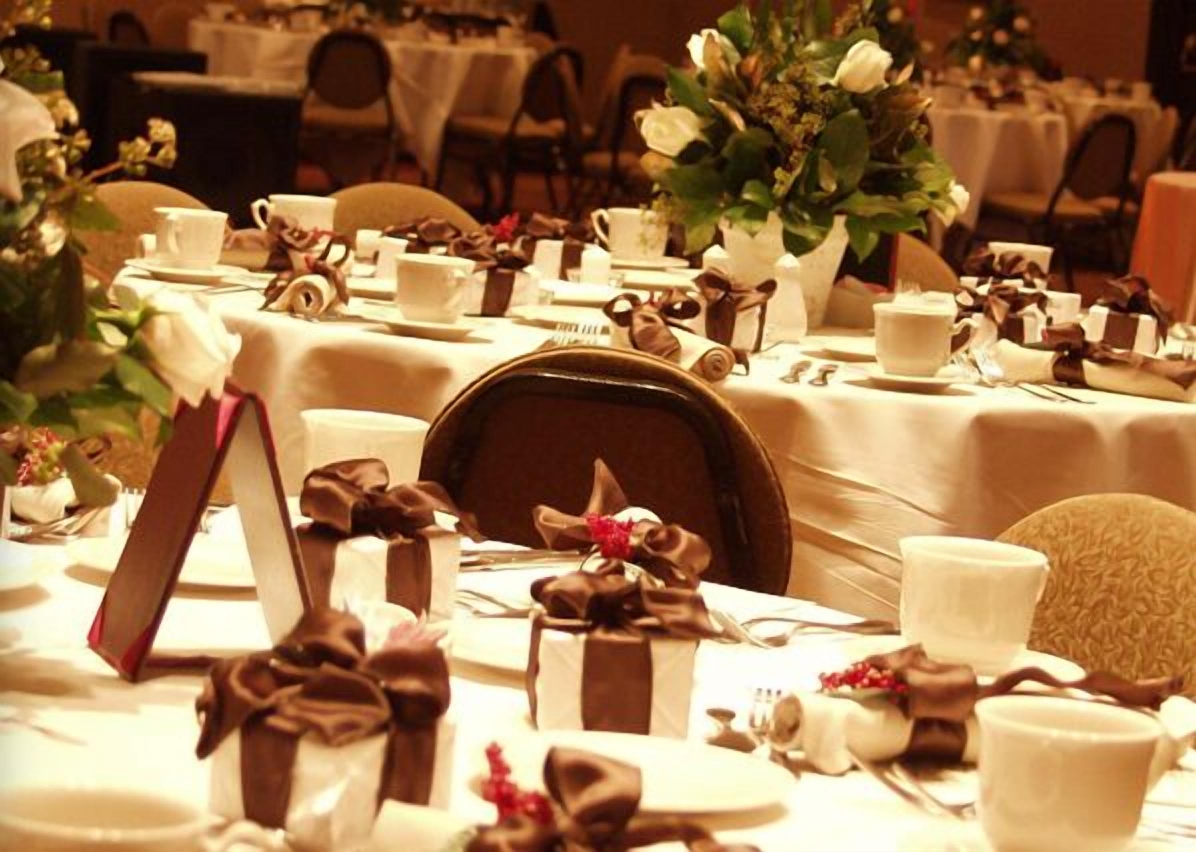 A banquet hall with tables set for a formal event, featuring white tablecloths, neatly arranged place settings, and floral centerpieces.