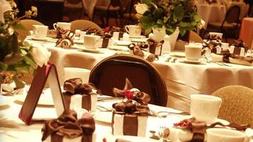 A banquet hall with tables set for a formal event, featuring white tablecloths, neatly arranged place settings, and floral centerpieces.