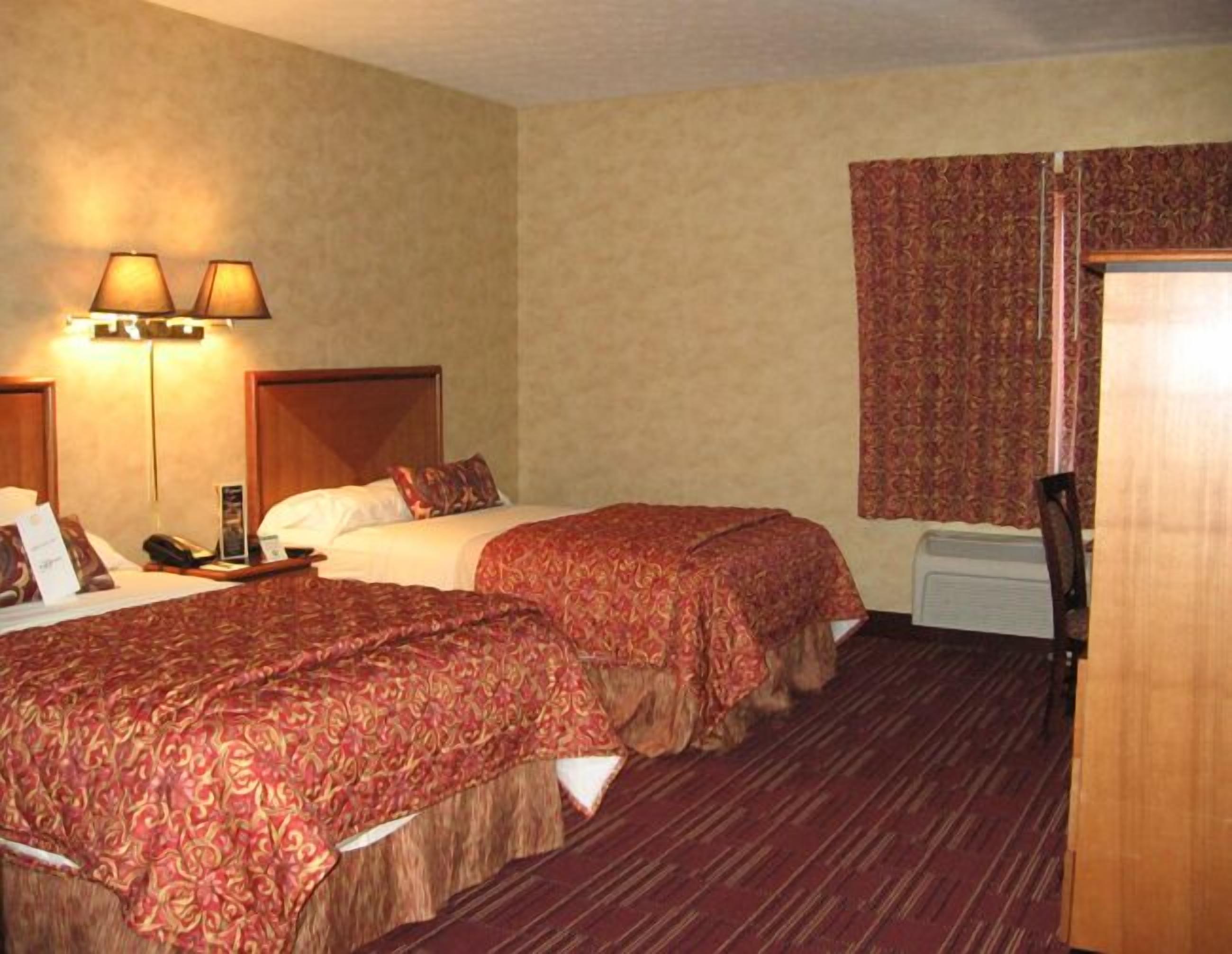 A hotel room with two beds, a wooden headboard, a telephone, a nightstand, and a window with curtains.