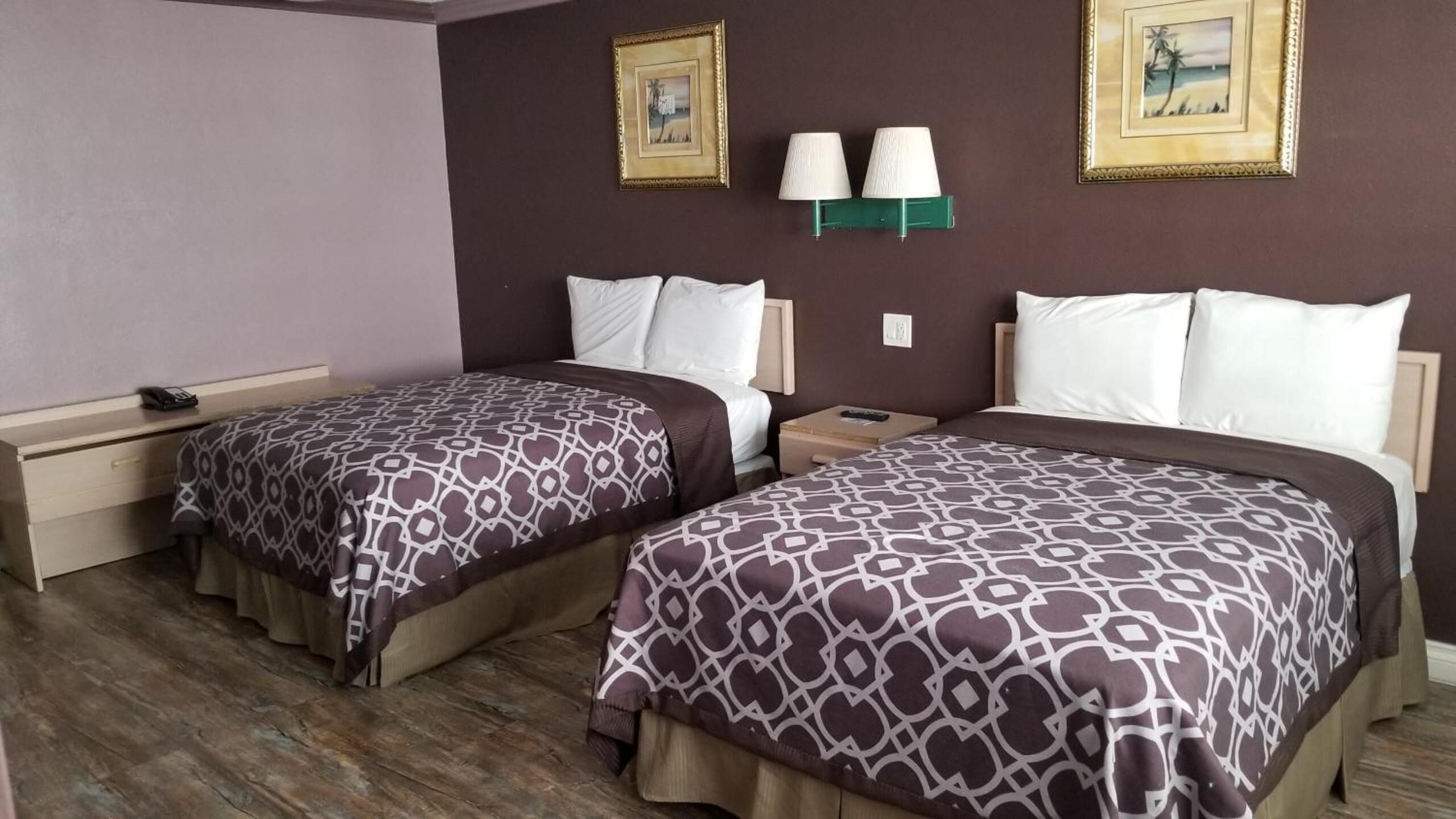 A hotel room with two beds, each with patterned bedding, a nightstand, a lamp, and two framed pictures on the wall.
