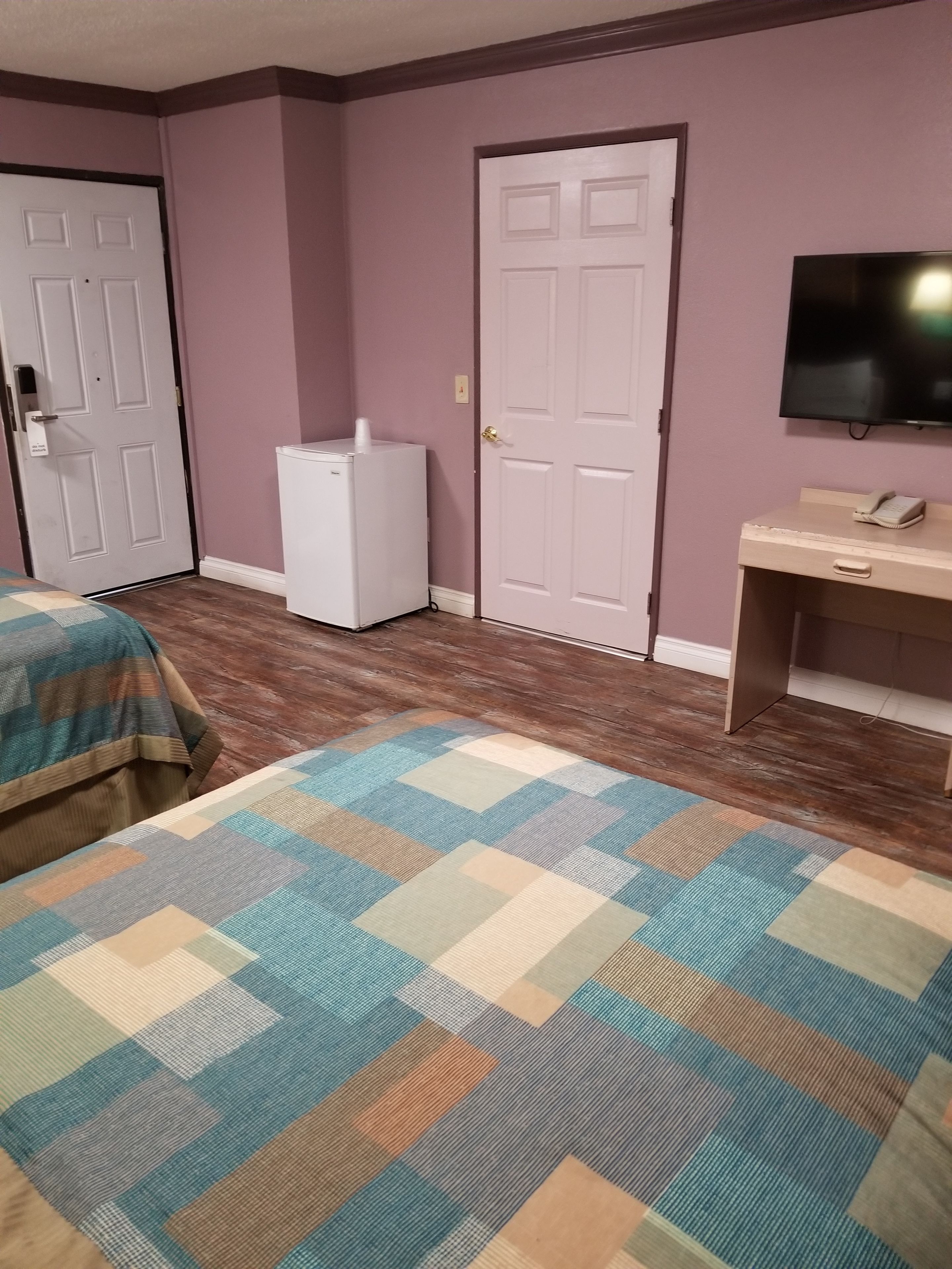 A hotel room with two beds, a desk, a television, and a refrigerator.