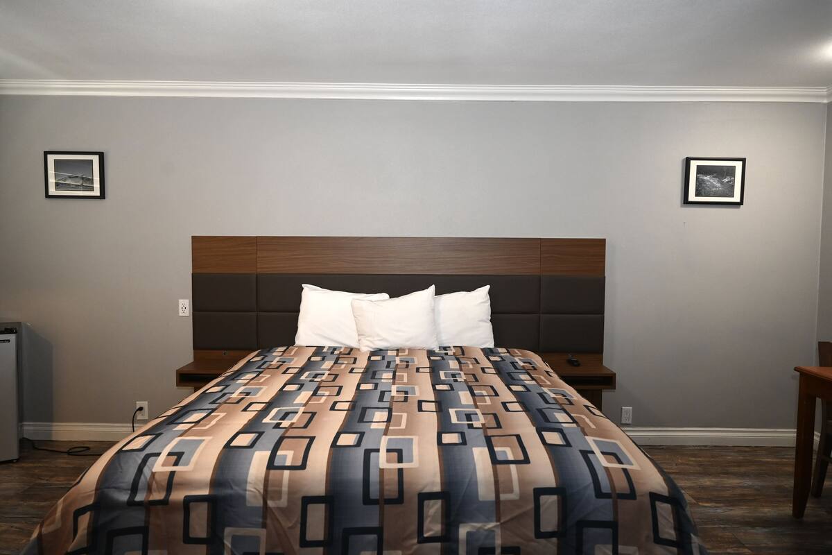 A hotel room with a large bed, a wooden headboard, two bedside tables, and a small desk.