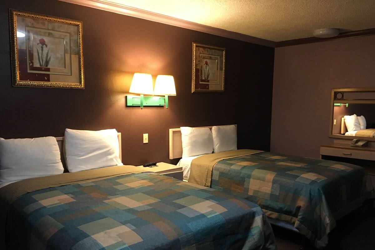 A hotel room with two beds, each with a checkered bedspread, two bedside lamps, and framed pictures on the wall.