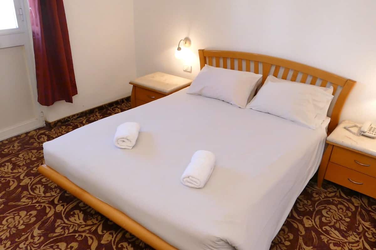 A neatly made bed with two rolled towels, a wooden headboard, and bedside lamps.
