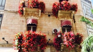 A building with a stone facade, multiple balconies with red flowers, and a tiled roof. - Zion Hotel (Jerusalem)