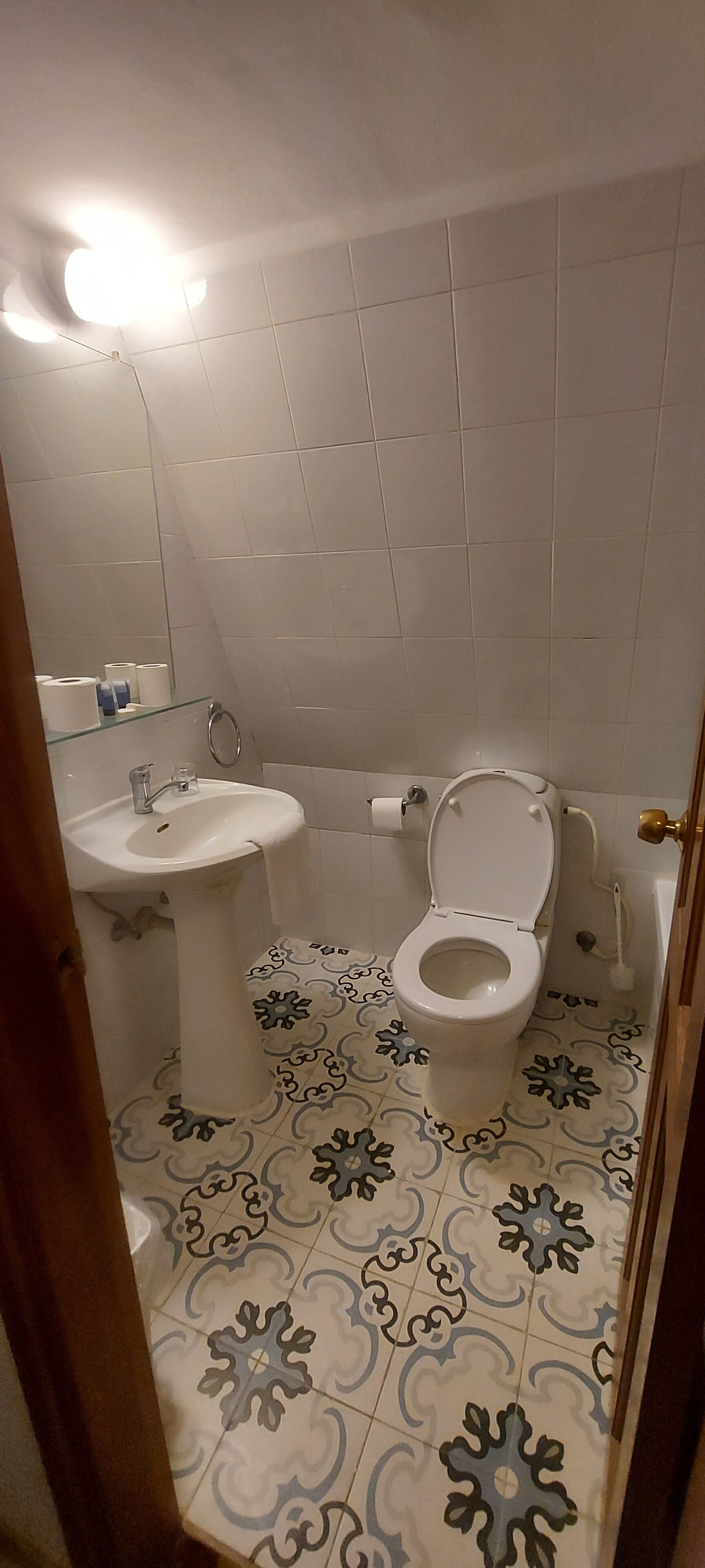 A bathroom with a toilet, sink, and patterned floor tiles.