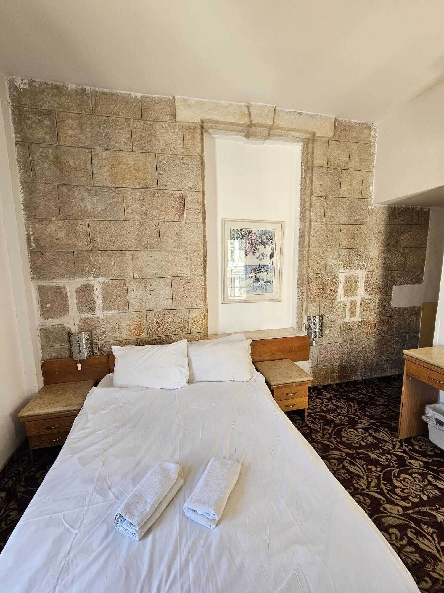 Ein Hotelzimmer mit einem großen Bett, einem Holz-Kopfteil, einer Steinwand und einem gerahmten Bild an der Wand.
