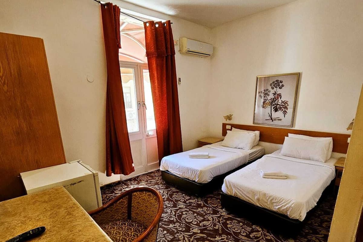 A hotel room with two beds, a desk, a chair, and a window with curtains.