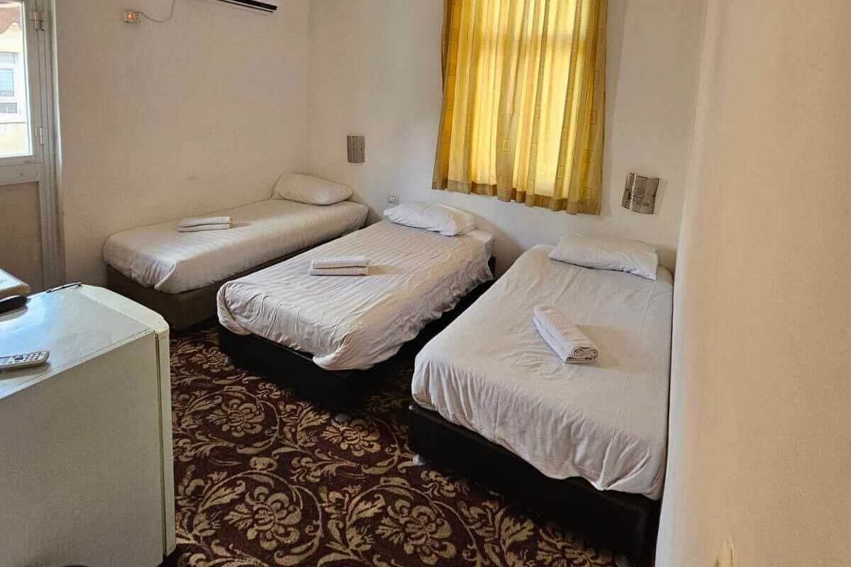 A small, clean room with three single beds, a desk, and an air conditioning unit.