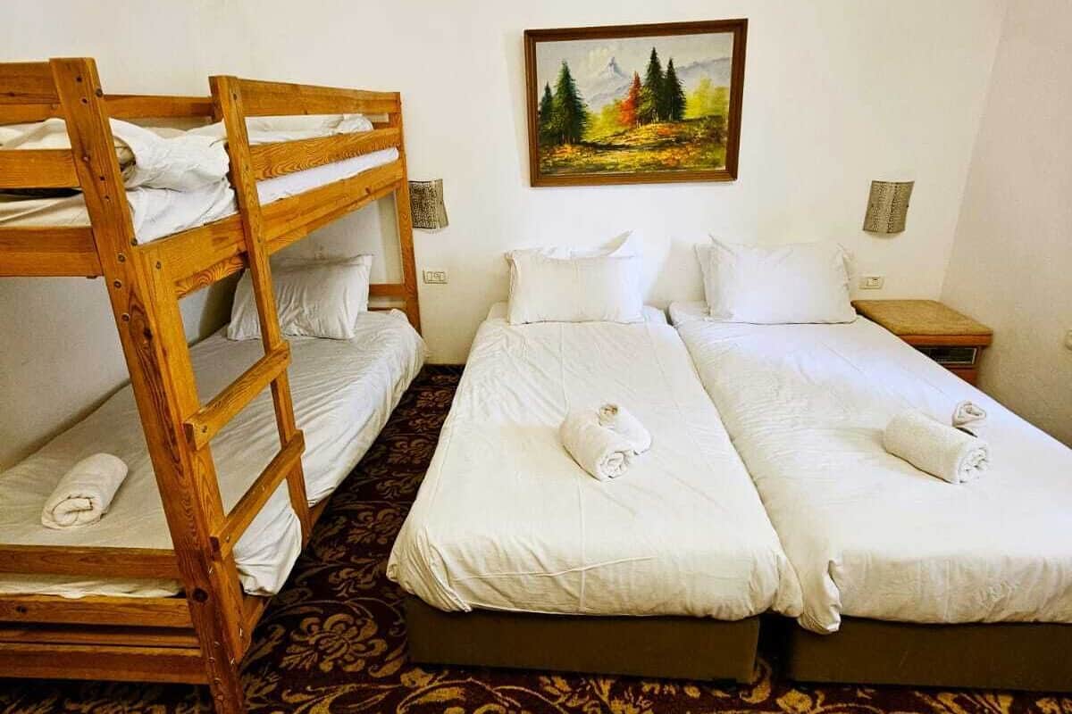 A hotel room with two single beds, a bunk bed, a painting on the wall, and a patterned carpet.