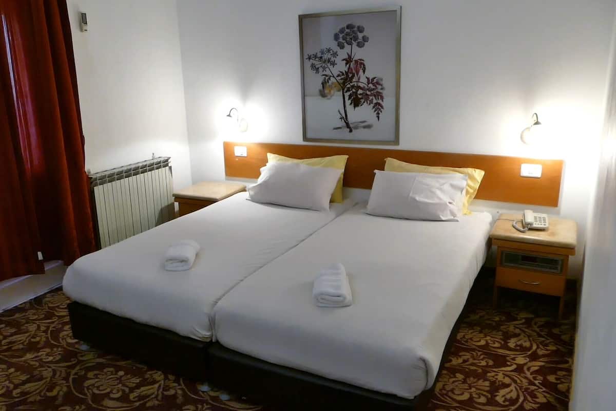 A double bed with white linens, two bedside tables with lamps, a radiator, and a floral artwork on the wall.