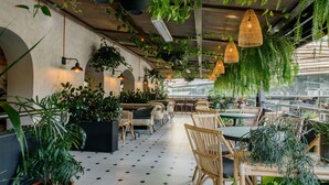 A restaurant with outdoor seating, potted plants, and hanging light fixtures.