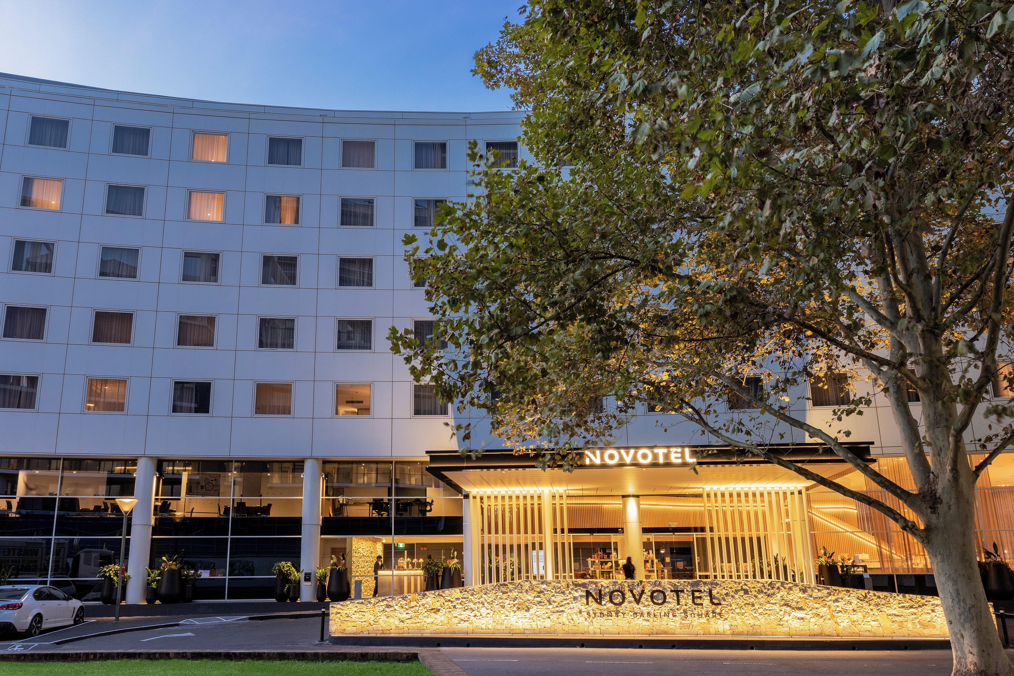A modern hotel with a curved facade, large windows, and a well-lit entrance.