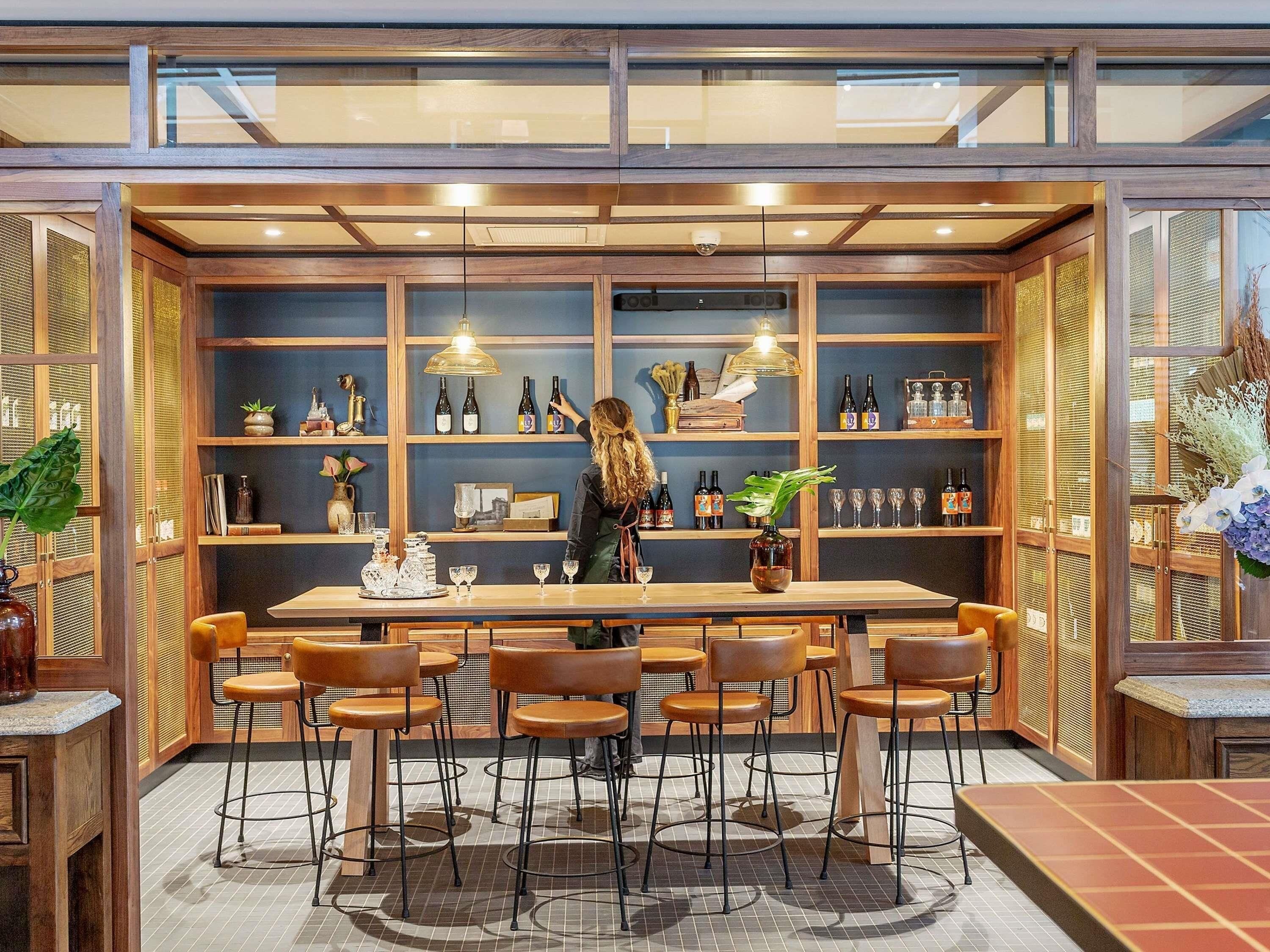 A bar area with a wooden bar counter, multiple shelves with bottles, and several stools.