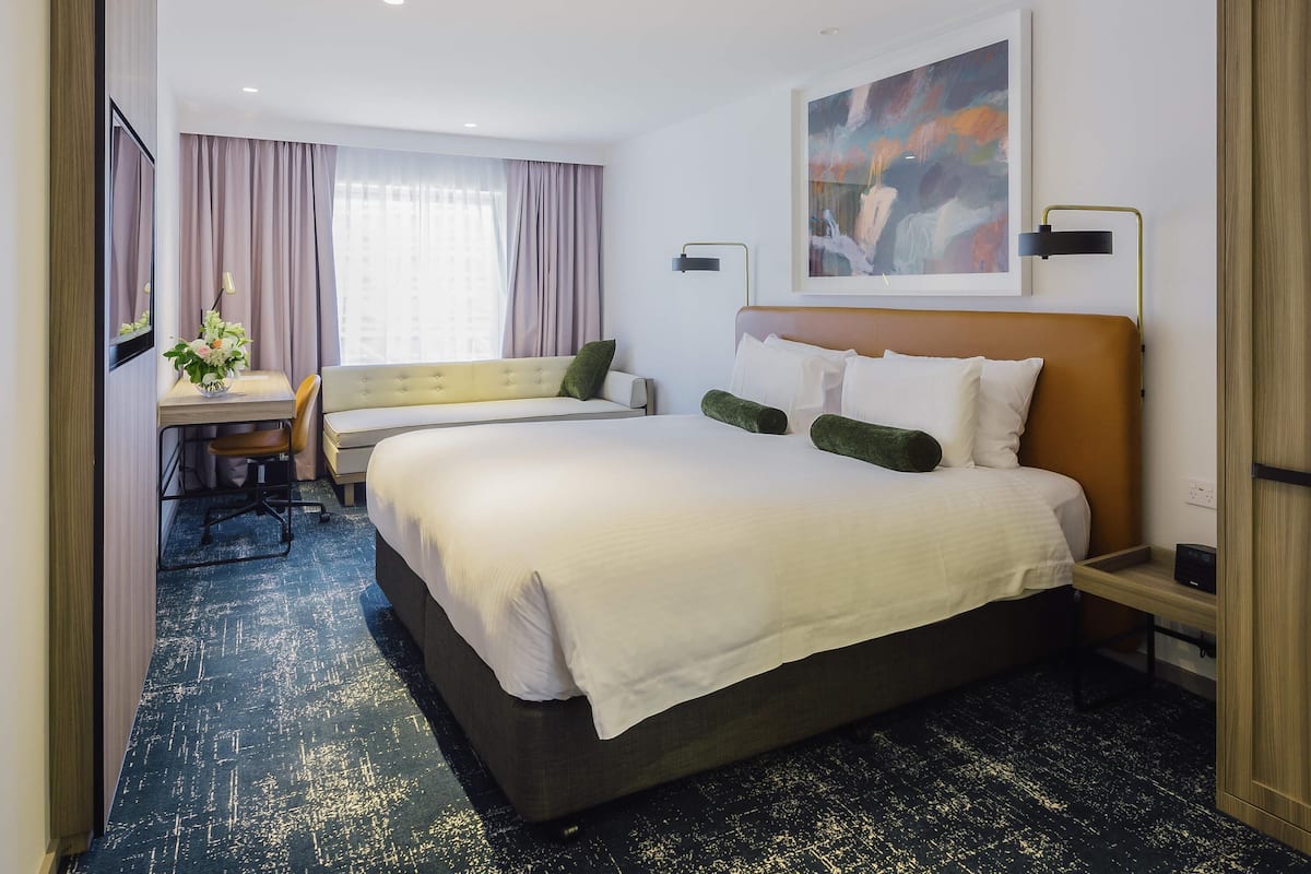 A hotel room with a large bed, a desk with a chair, a sofa, and a painting on the wall.