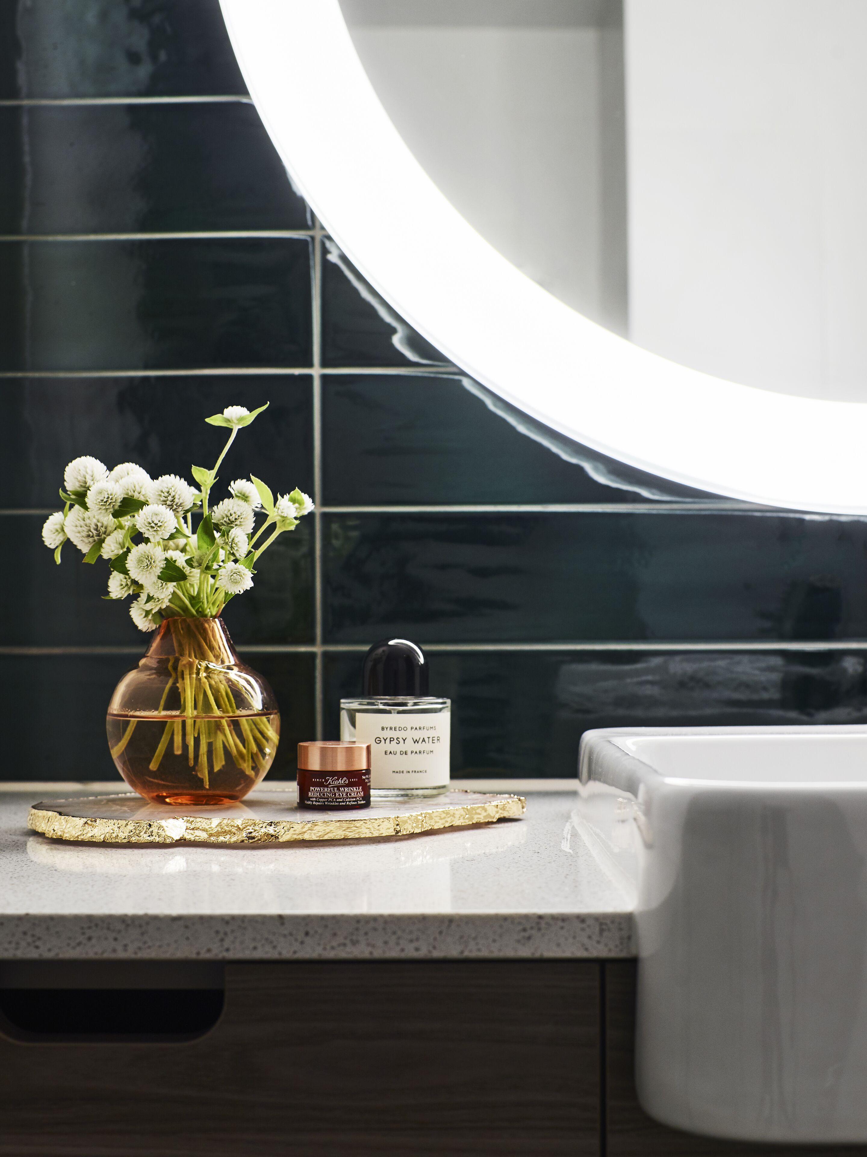 A bathroom vanity with a vase of white flowers, a perfume bottle, and a small container.