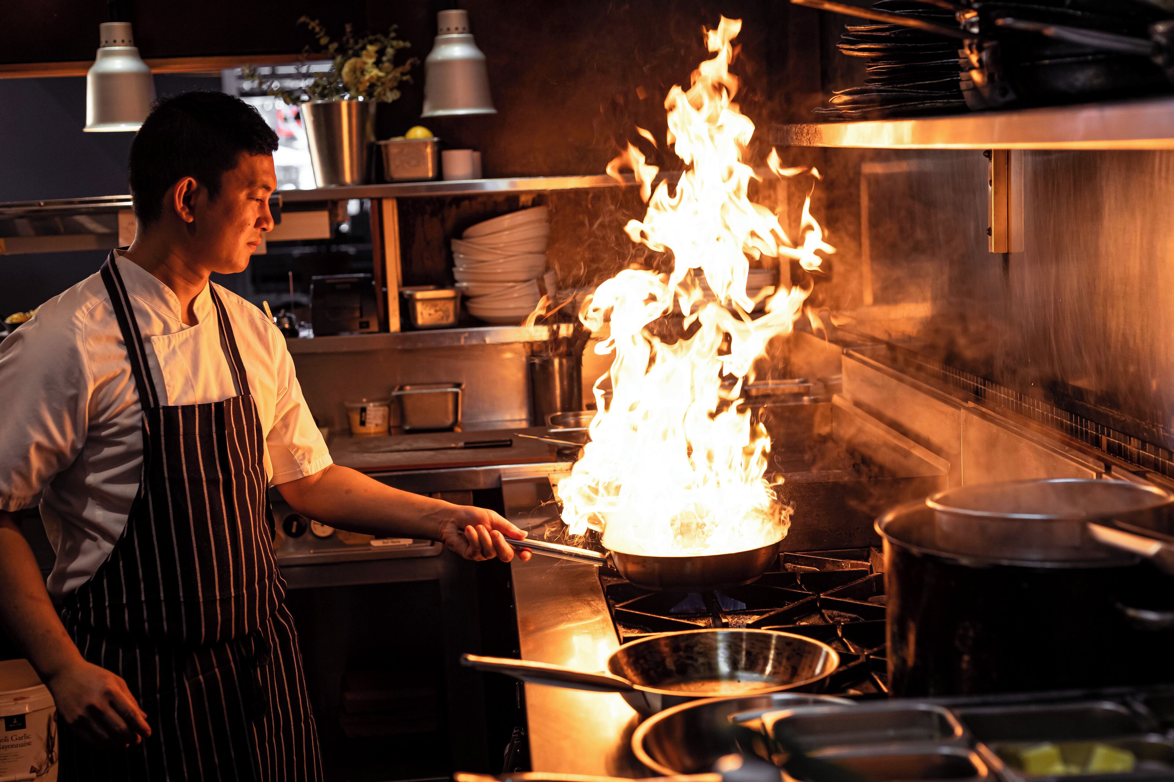 A chef cooking with a pan on a stove with flames.