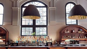 A bar with wooden furnishings, a variety of liquor bottles, and large arched windows.