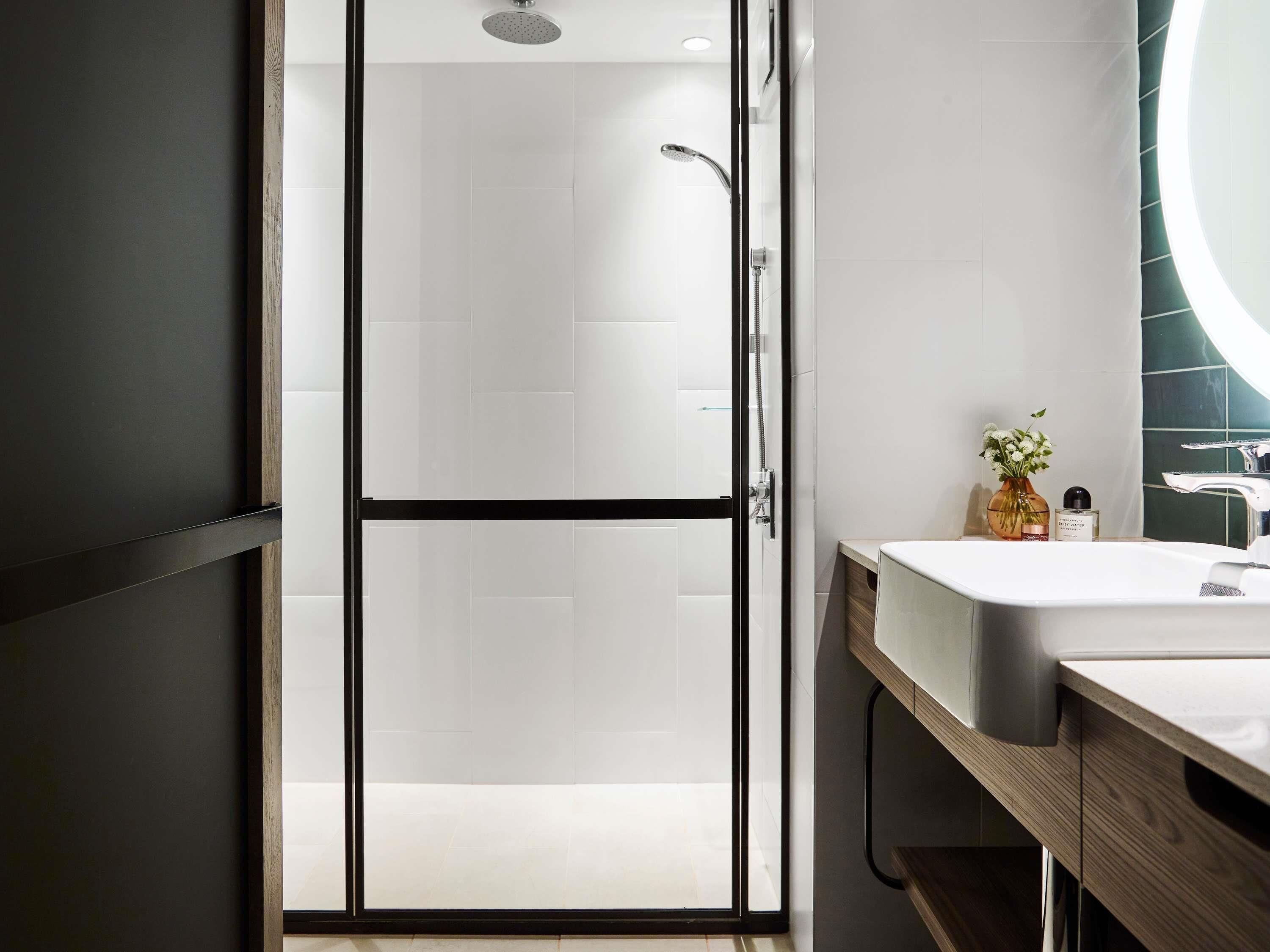 Une salle de bain moderne avec une porte de douche en verre, un lavabo blanc et un meuble-lavabo en bois.