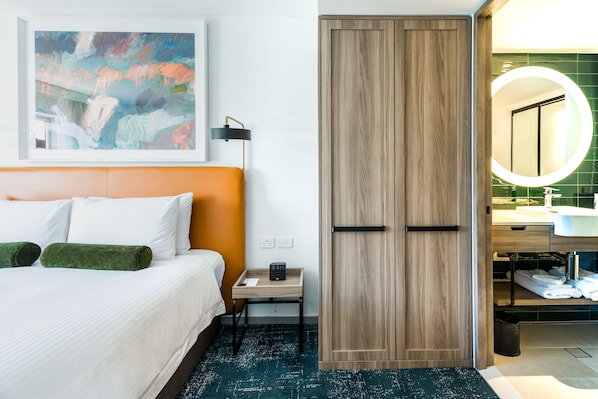Une chambre d’hôtel avec un lit, une table de chevet, une armoire en bois et une salle de bain équipée d’un miroir et d’un lavabo.