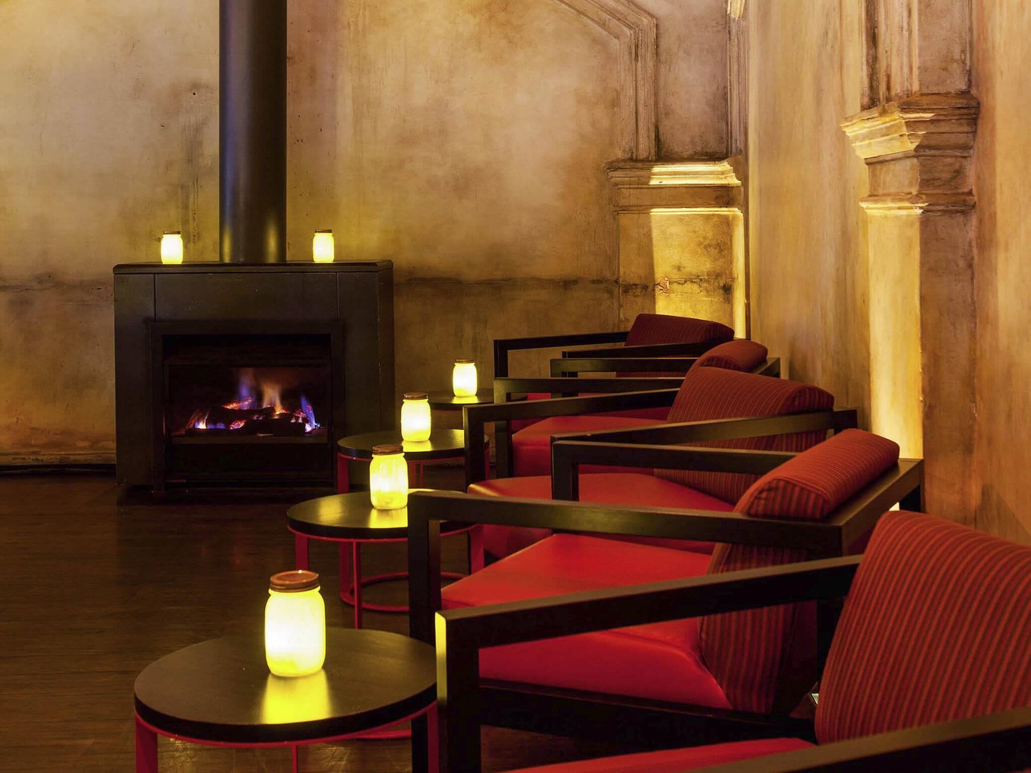 A cozy lounge area with a fireplace, red upholstered chairs, and small tables with candles.