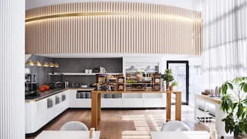 A modern kitchen with a curved wooden panel ceiling, a central island with various food items, and a view of the city through large windows.