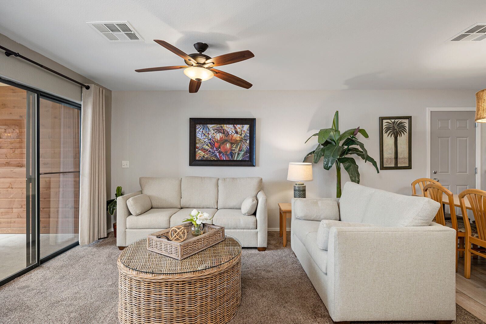 A living room with two sofas, a round wicker coffee table, a ceiling fan, and a large plant.