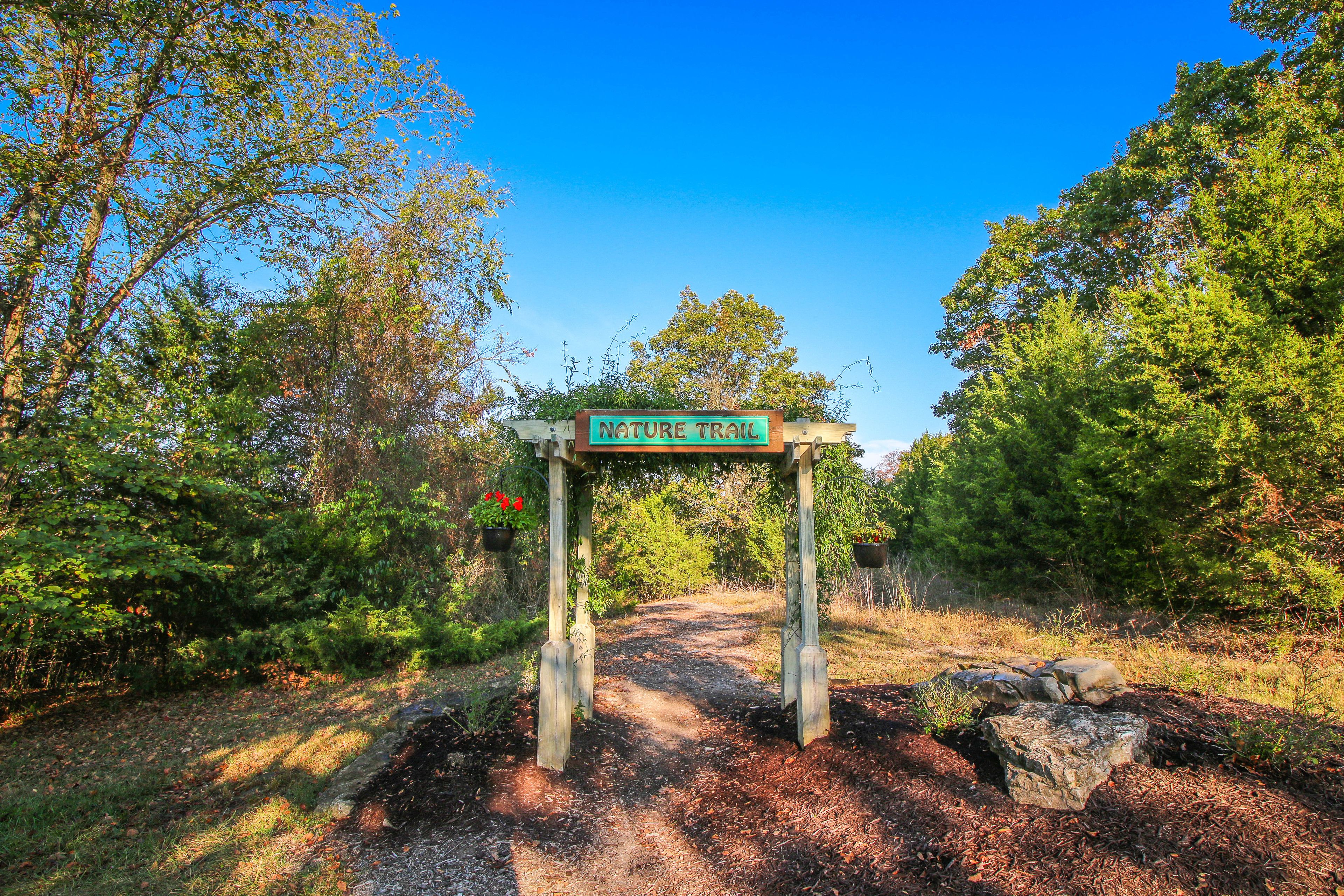 A nature trail sign with a wooden archway, surrounded by trees and a clear sky.