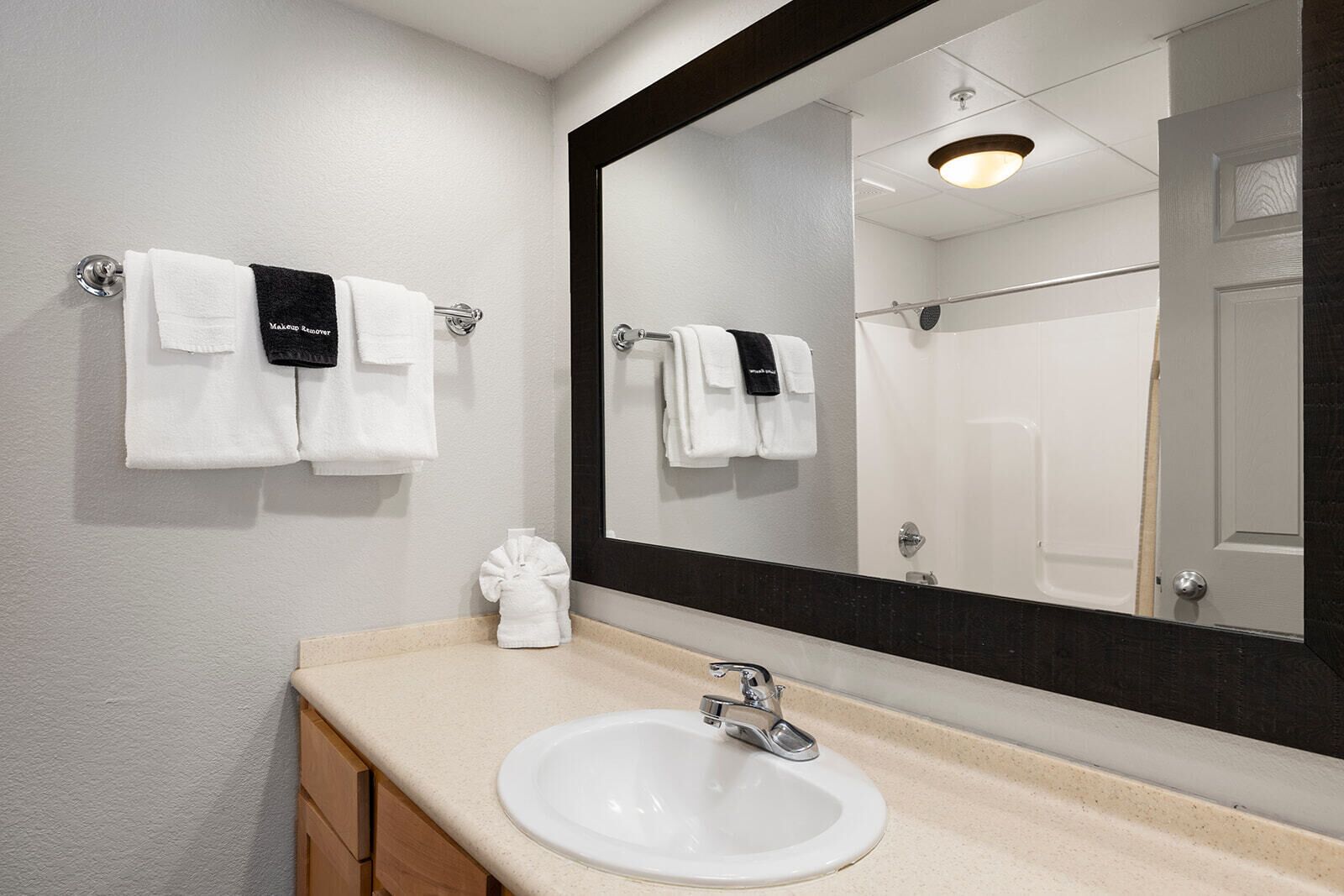 Un baño con un lavamanos blanco, un espejo grande y dos toallas colgadas en ganchos.