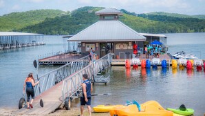 A dock with a small building, paddle boats, and a lake with hills in the background. - Still Waters Resort (Branson)