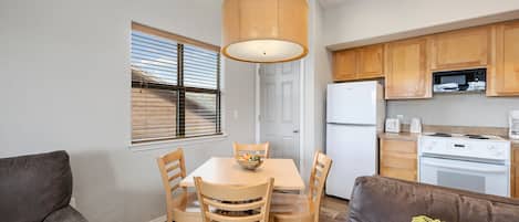 Una cocina compacta con armarios de madera, un refrigerador blanco, un microondas, una estufa y un comedor con mesa y sillas.