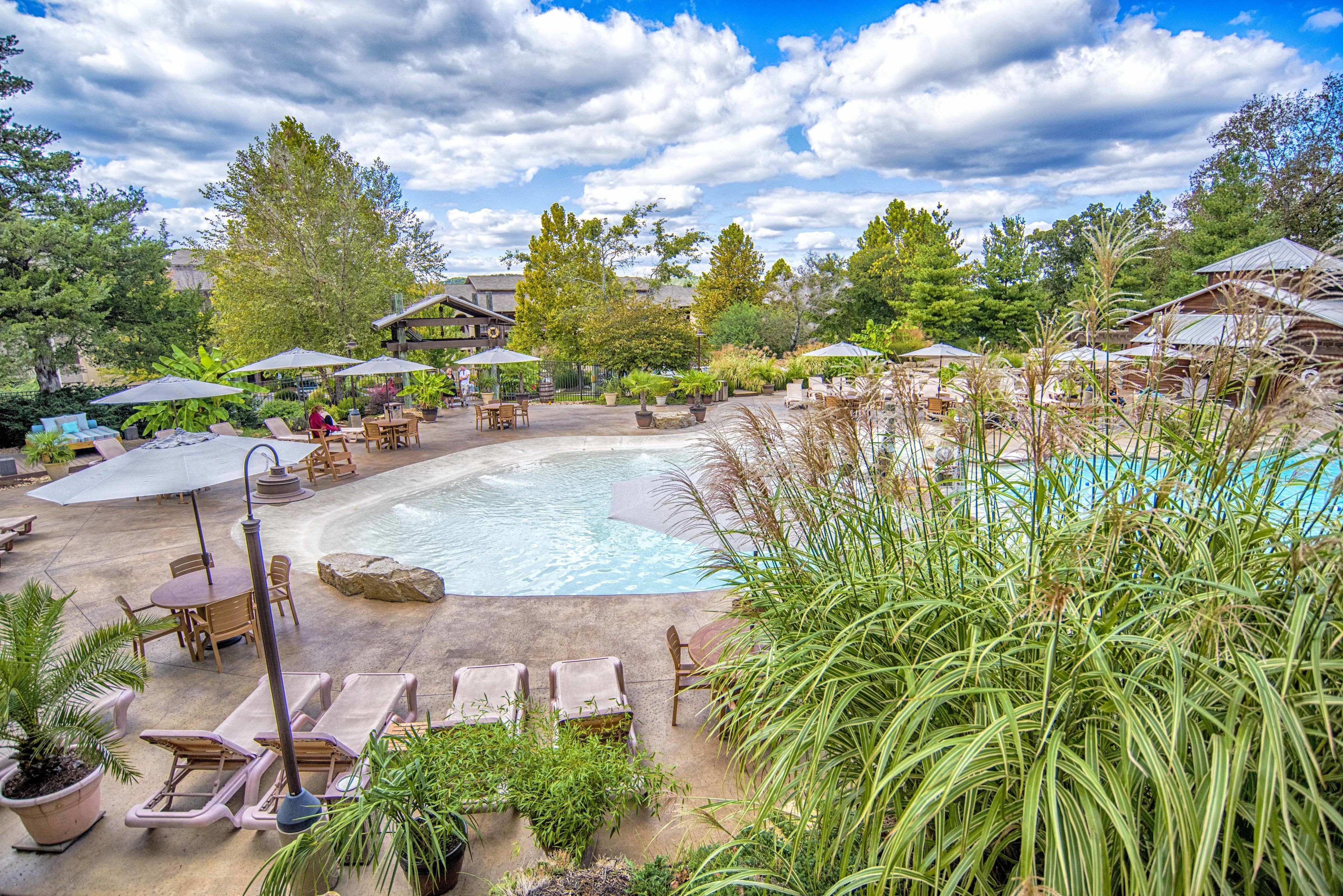 A resort with a swimming pool, outdoor seating, and lush greenery.