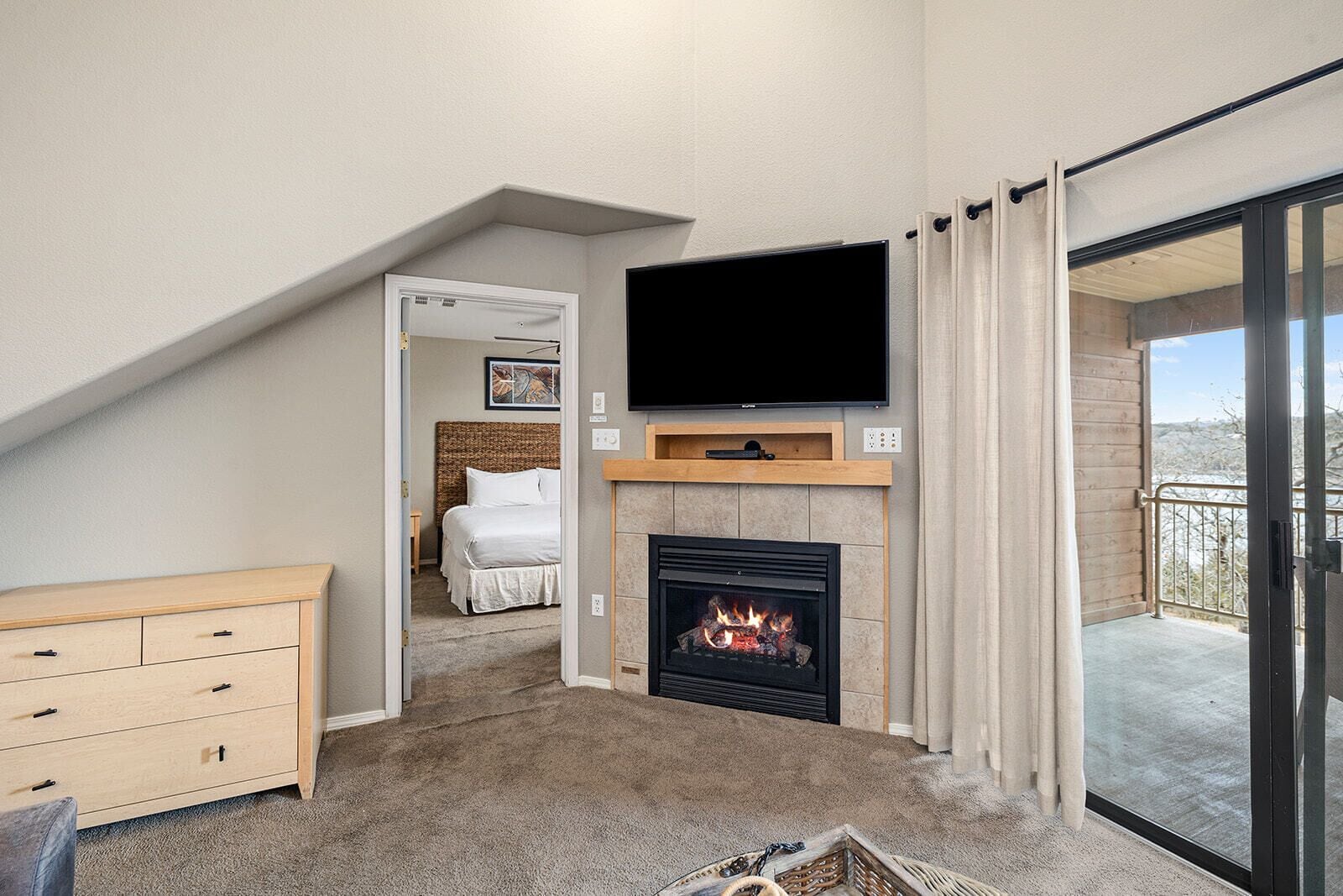 A bedroom with a fireplace, a TV mounted above it, and a balcony with a view.