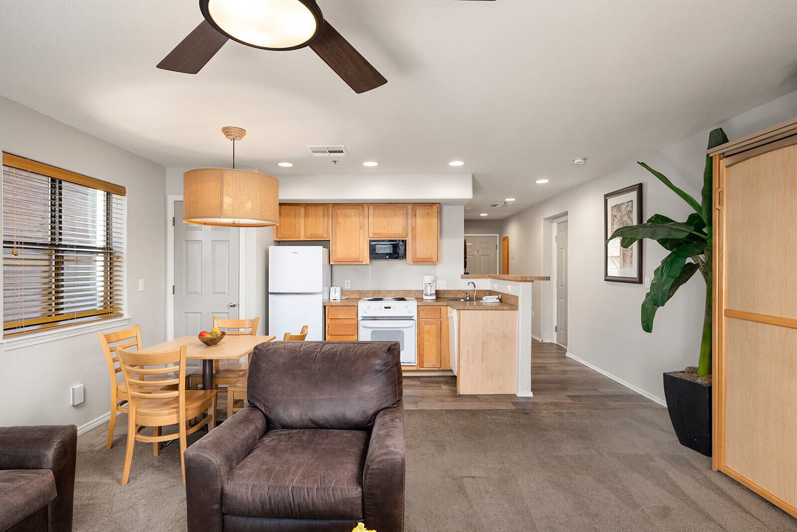 A modern kitchen with wooden cabinets, a refrigerator, stove, and a dining area with a table and chairs.