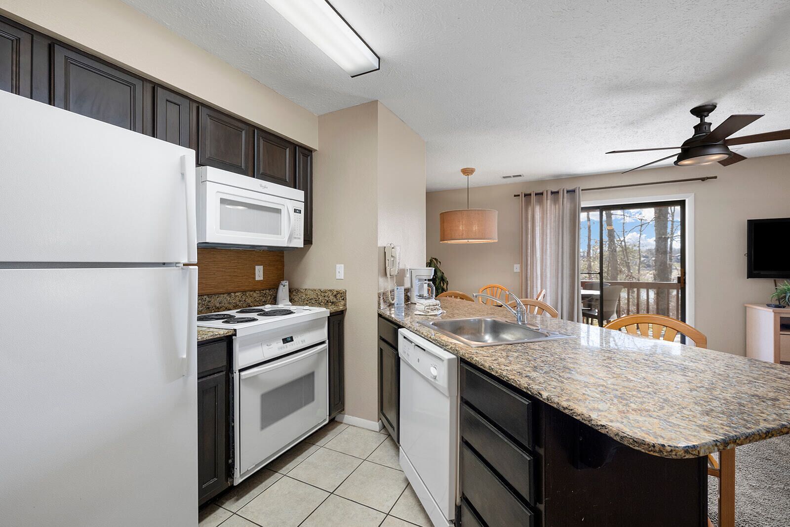 A compact kitchen with a microwave, stove, dishwasher, and granite countertop.