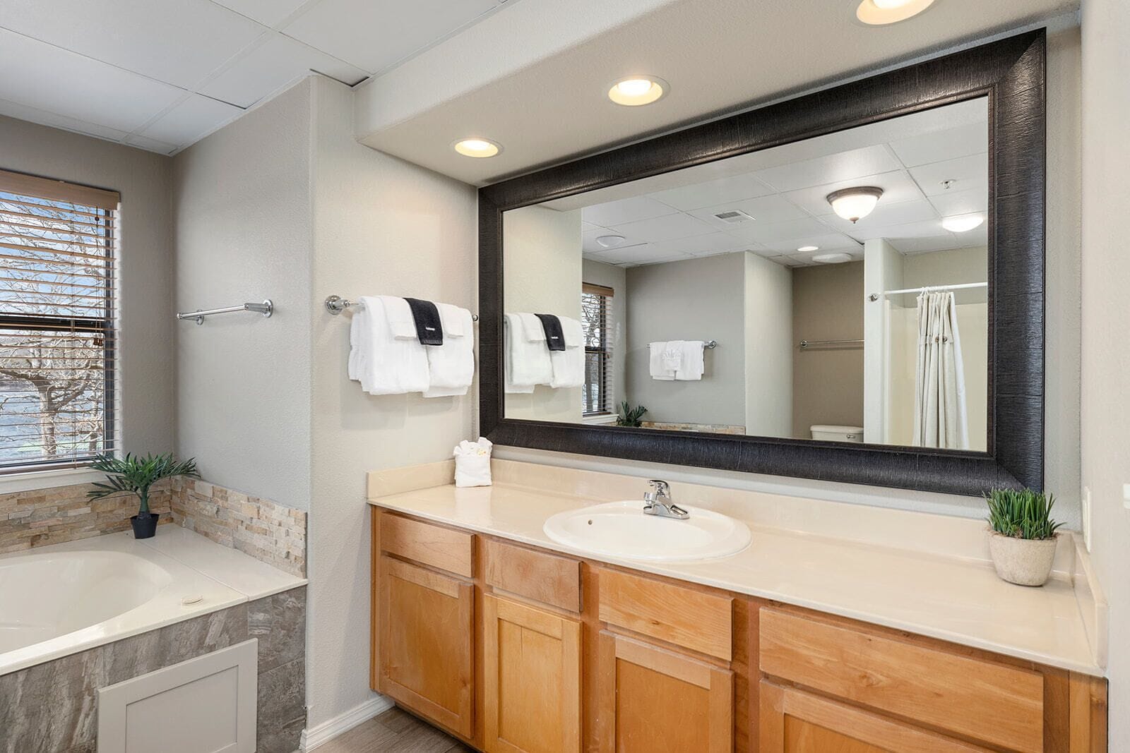 A modern bathroom with a large mirror, a bathtub, a sink, and wooden cabinets.